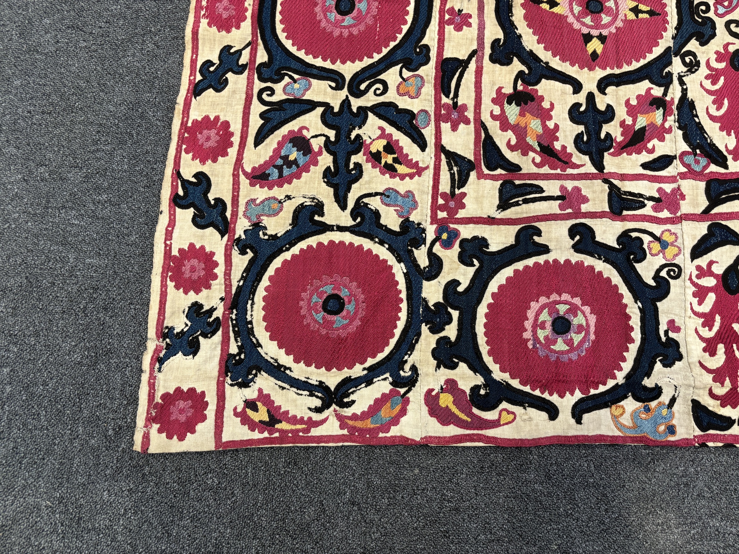 An 19th century Uzbek Suzani embroidered wall hanging, in two pieces, the main hanging sewn together as four panels, together with a fifth matching border, being detached, embroidered with large bold floral motifs, in ri